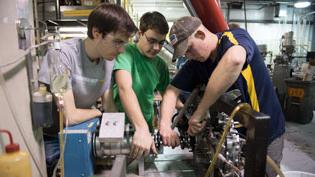 Three males work on engine